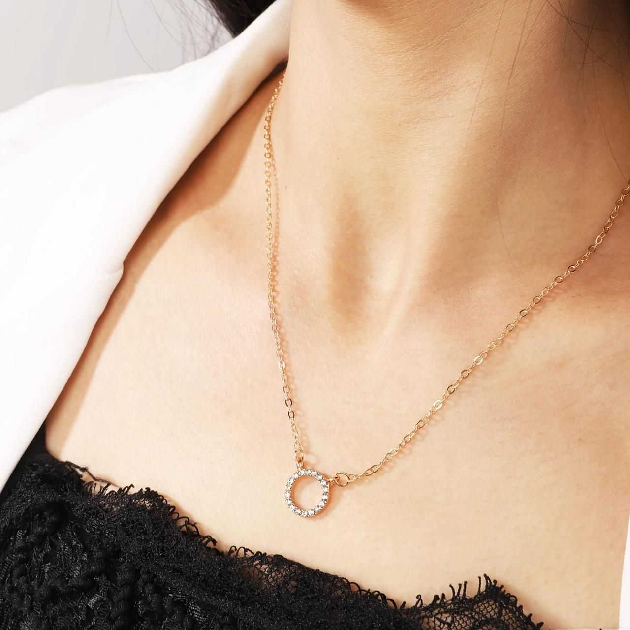 Rose gold necklace with a circular pendant on a person wearing a black lace top.